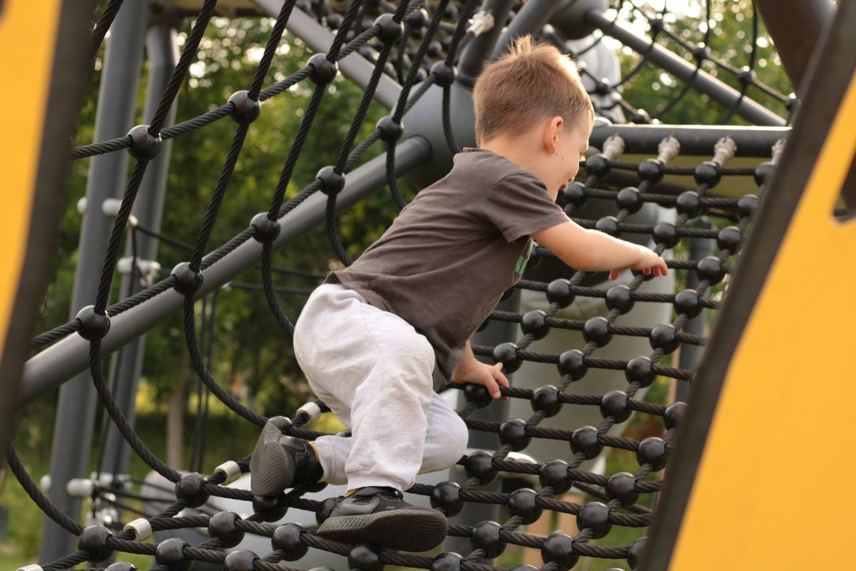 safe climbing toys for toddlers featuring padded gloves on a toddler gripping a wooden climbing wall